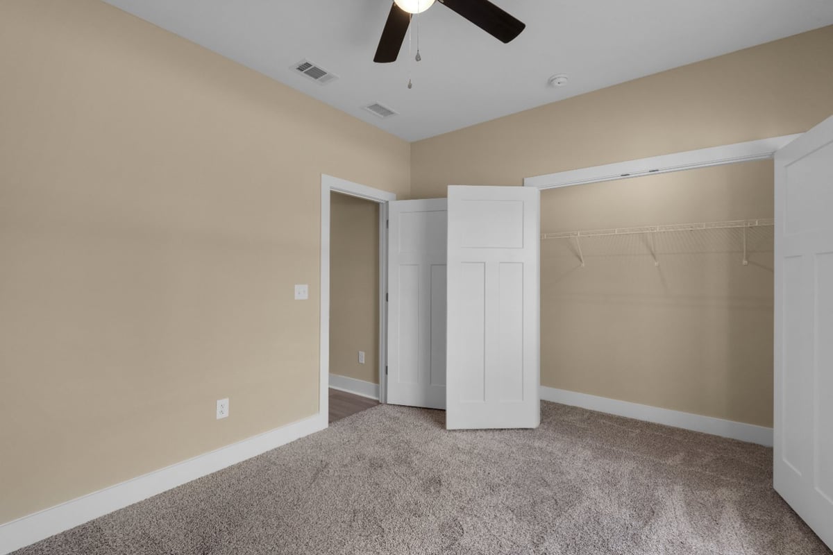 bedroom with open closet and carpet flooring in The Poderosa custom home by EZ Modern Homes Pensacola, FL-optimized