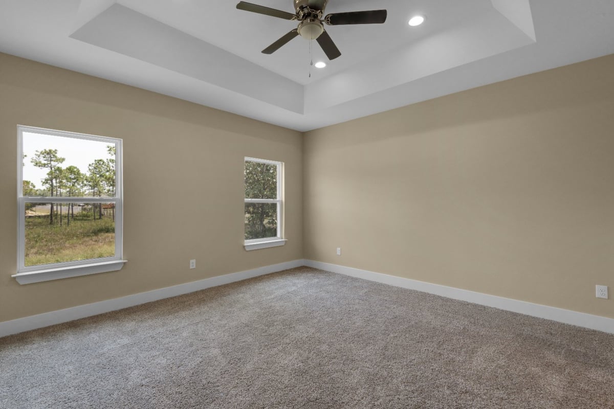 carpeted bedroom with tray ceiling and ceiling fan in Pensacola FL custom home by EZ Modern Homes The Poderosa-optimized