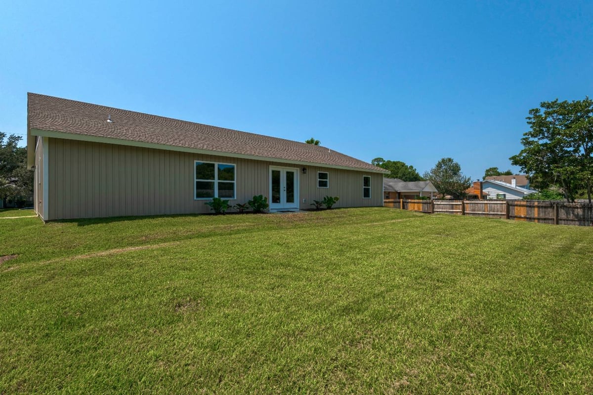 angled backyard view of custom home exterior with fence and lawn by EZ Modern Homes in Pensacola, FL-optimized
