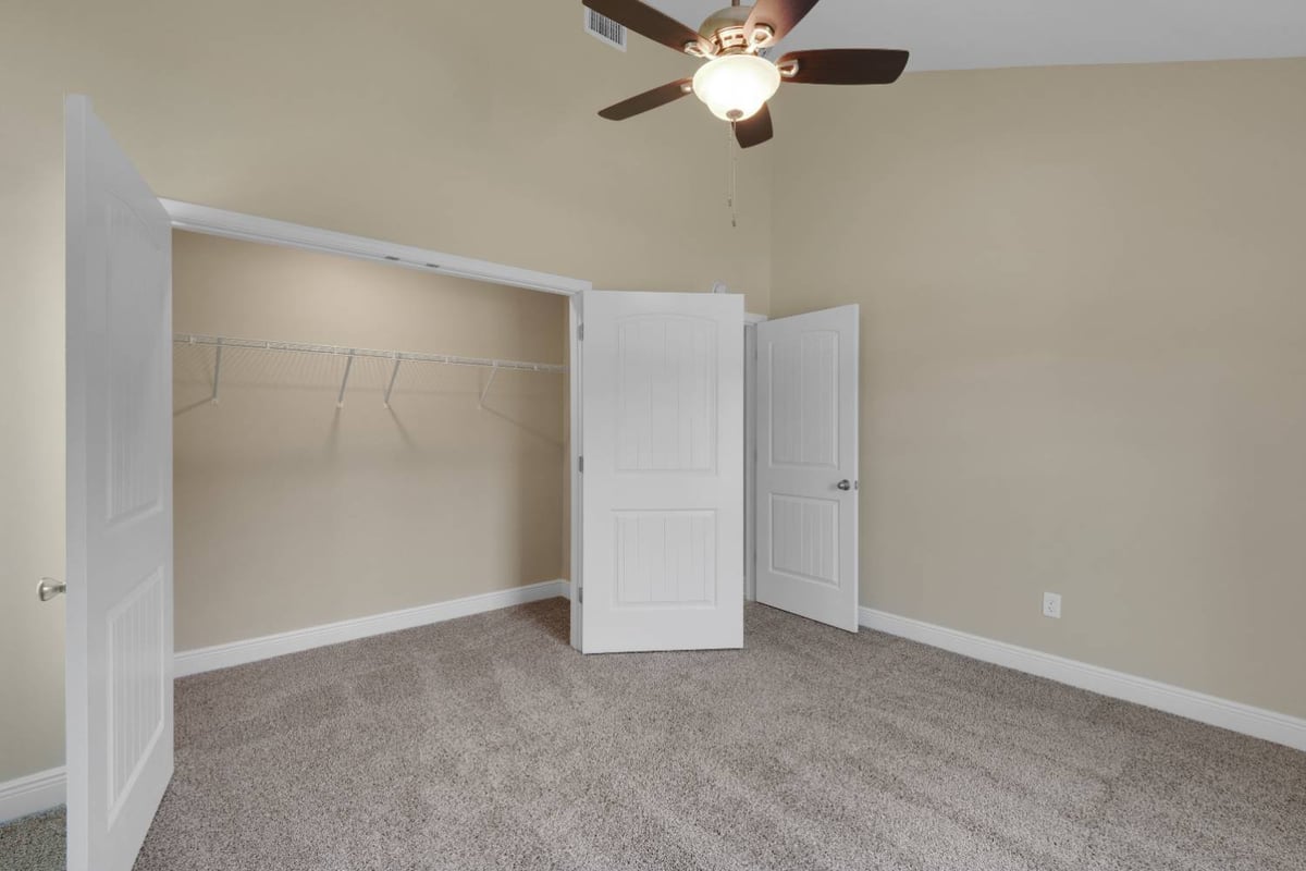 bedroom with walk-in closet and ceiling fan in custom home by EZ Modern Homes in Pensacola, FL-optimized