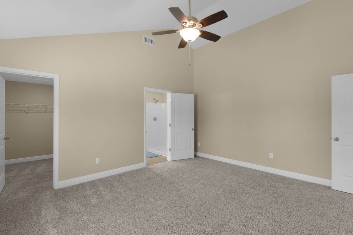 spacious custom home bedroom with vaulted ceiling, carpet flooring, and ensuite access by EZ Modern Homes in Pensacola, FL-optimized