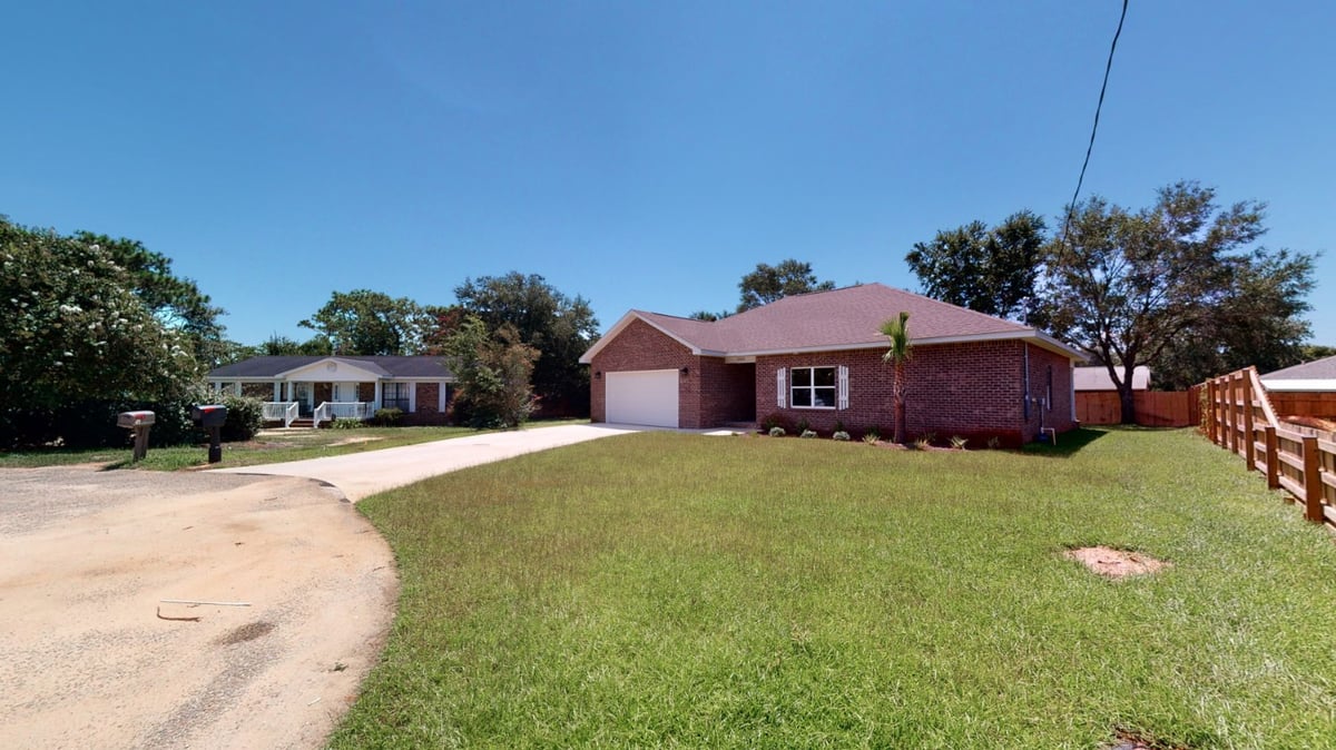 Angled exterior view of a custom home by EZ Modern Homes in Pensacola, FL with large yard and side fencing.-optimized