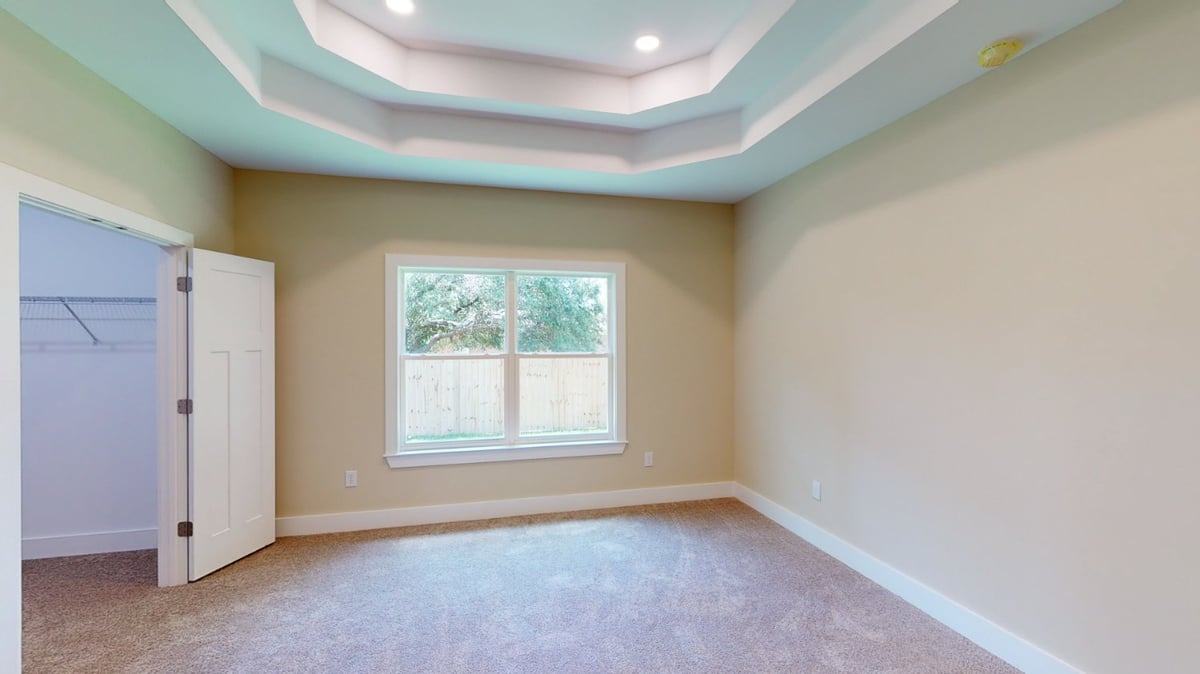 bedroom with tray ceiling, window, and walk-in closet in custom home by EZ Modern Homes Pensacola, FL-optimized