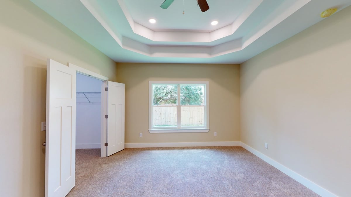 bright carpeted bedroom with tray ceiling and window in custom home by EZ Modern Homes in Pensacola, FL-optimized