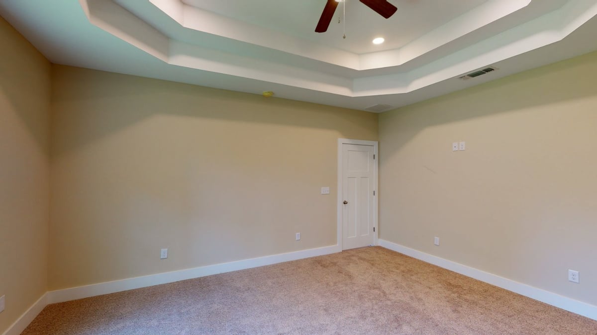 carpeted bedroom with ceiling detail and entry door in Pensacola, FL custom home by EZ Modern Homes-optimized