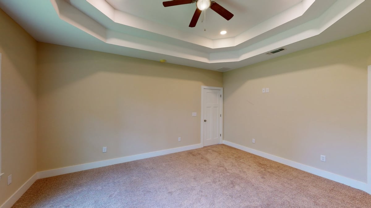 carpeted bedroom with tray ceiling and ceiling fan in custom home by EZ Modern Homes Pensacola, FL-optimized