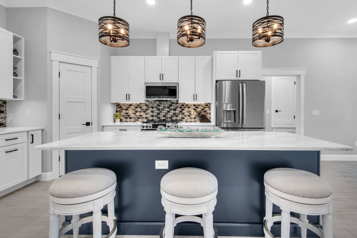Front view of large kitchen island with seating and pendant lights in The Lafon custom home by EZ Modern Homes Pensacola, FL-optimized